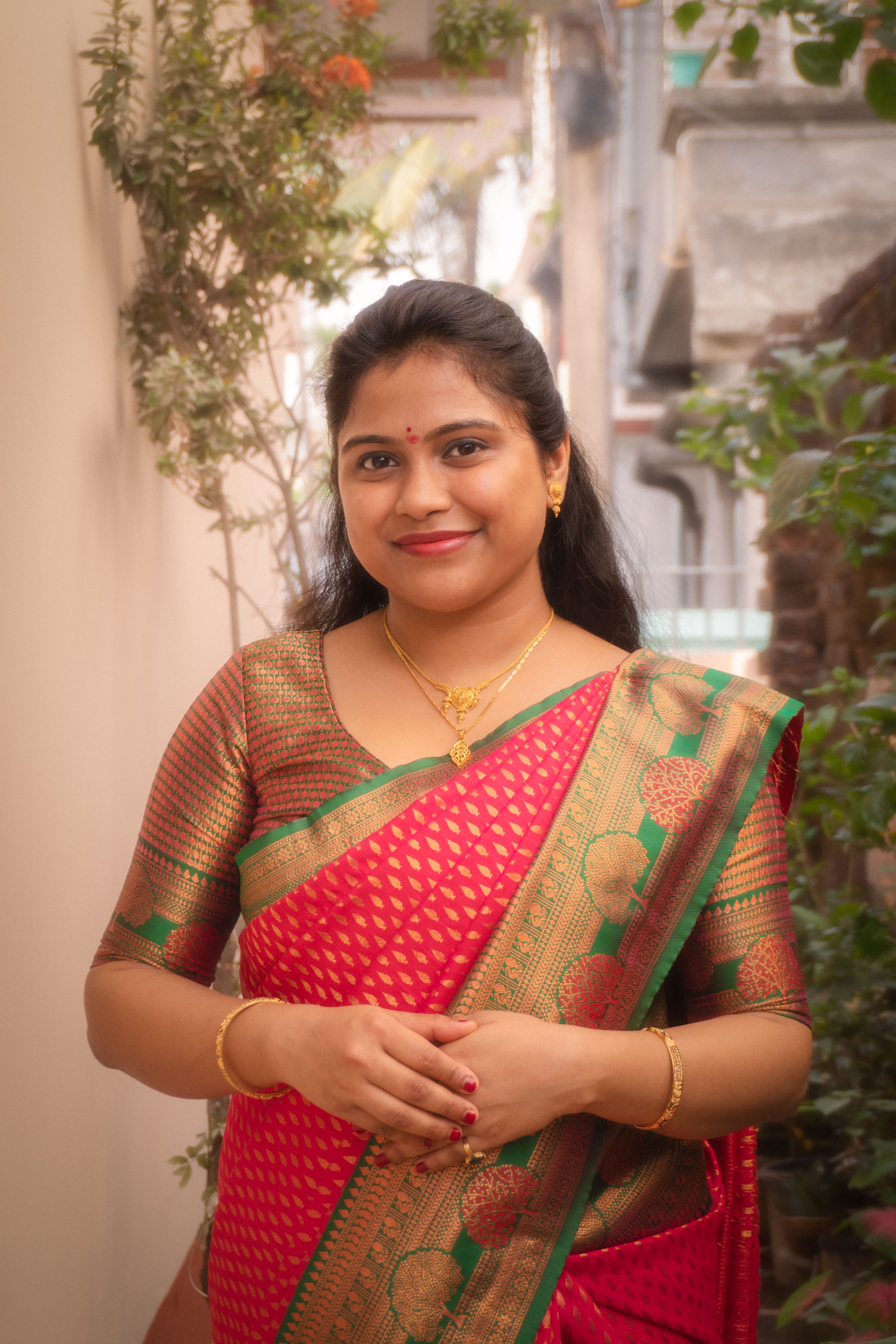 Smiling Indian woman in a red sari standing outside, embracing cultural elegance.