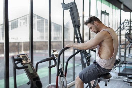 Side view of muscular male in sportswear training on exercise bike in modern fitness center