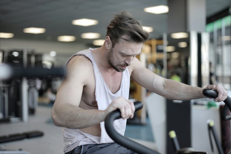 Tired Sportsman Exercising Bike In Gym