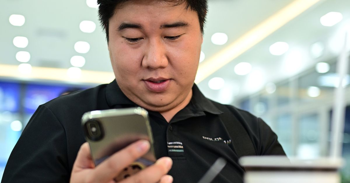 A man uses his smartphone while enjoying coffee indoors, showcasing a modern digital lifestyle.