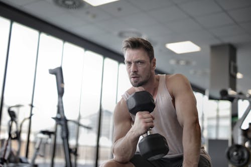 Free Muscular athletic man exercising with dumbbell in sports center Stock Photo