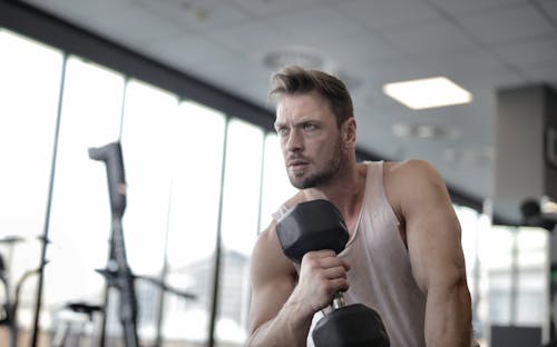 Free Man in White Tank Top Holding Black Dumbbell Stock Photo