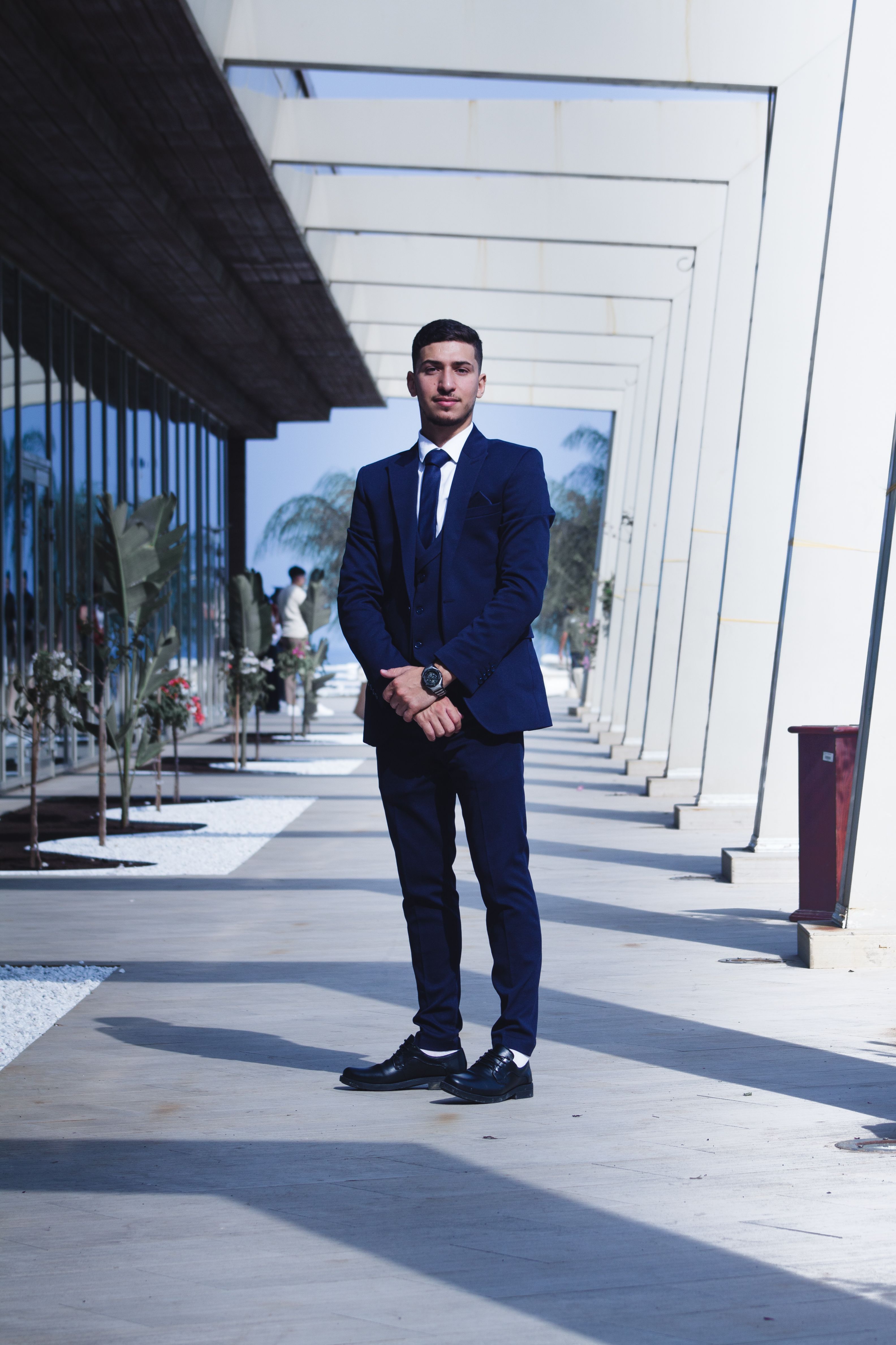 A young man confidently posing in a blue suit in a modern architectural outdoor setting.