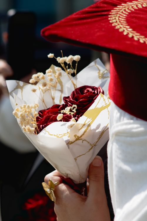 Free A graduate holding a bouquet of red roses during a ceremony, symbolizing achievement and success. Stock Photo