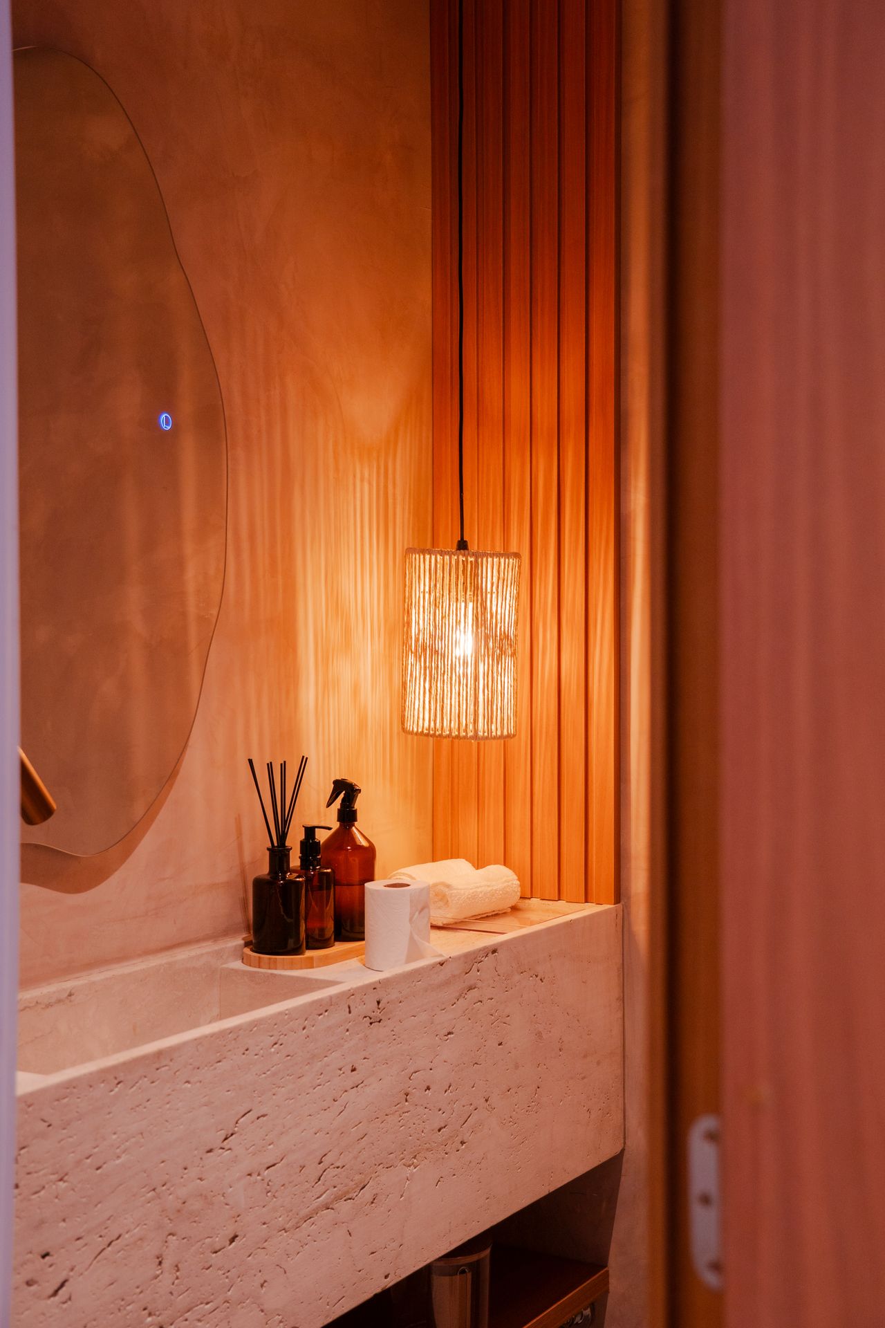 Woven rattan cylinder pendant light hanging in a warm terracotta toned bathroom vanity area