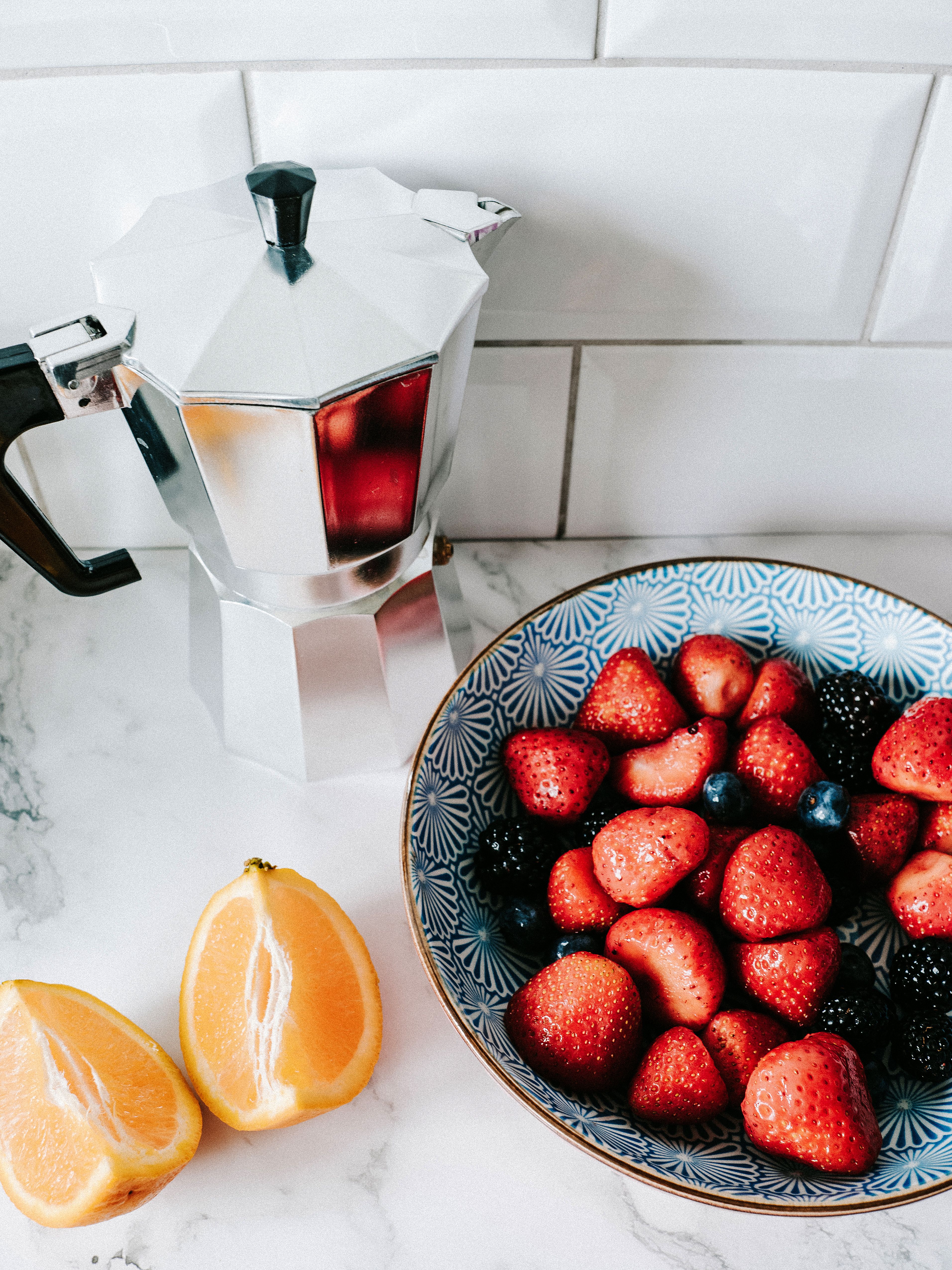 A vibrant breakfast setup featuring a moka pot, fresh fruits including strawberries and oranges.