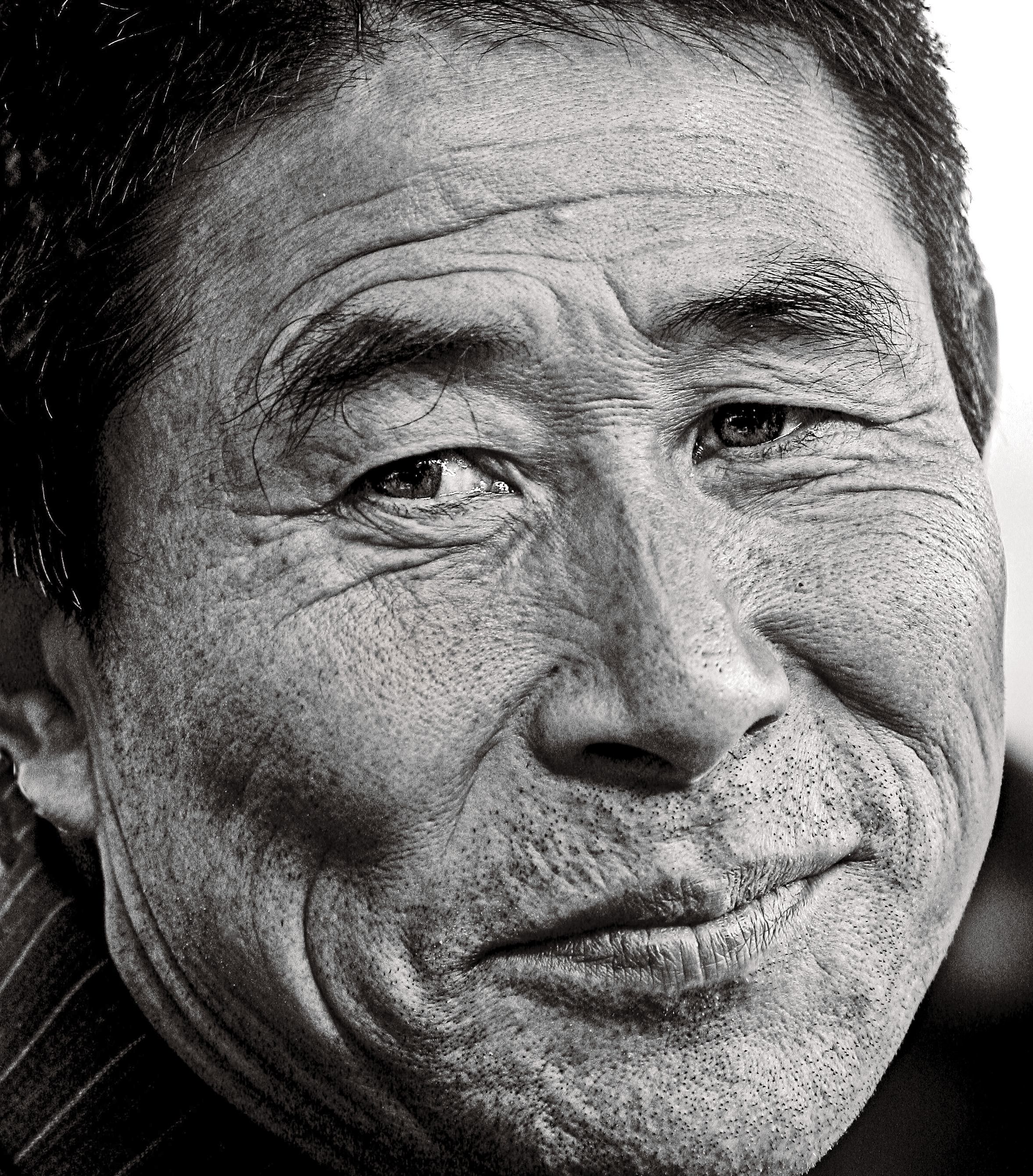 Close-up black and white portrait of an older man's expressive face with a gentle smile.