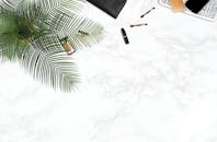 化妆用品以装饰性棕榈叶为特色，平躺在白色大理石背景上，显得时尚