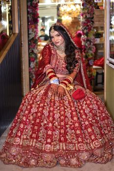 Smiling bride in exquisite red lehenga, showcasing intricate embroidery and traditional bridal jewelry.