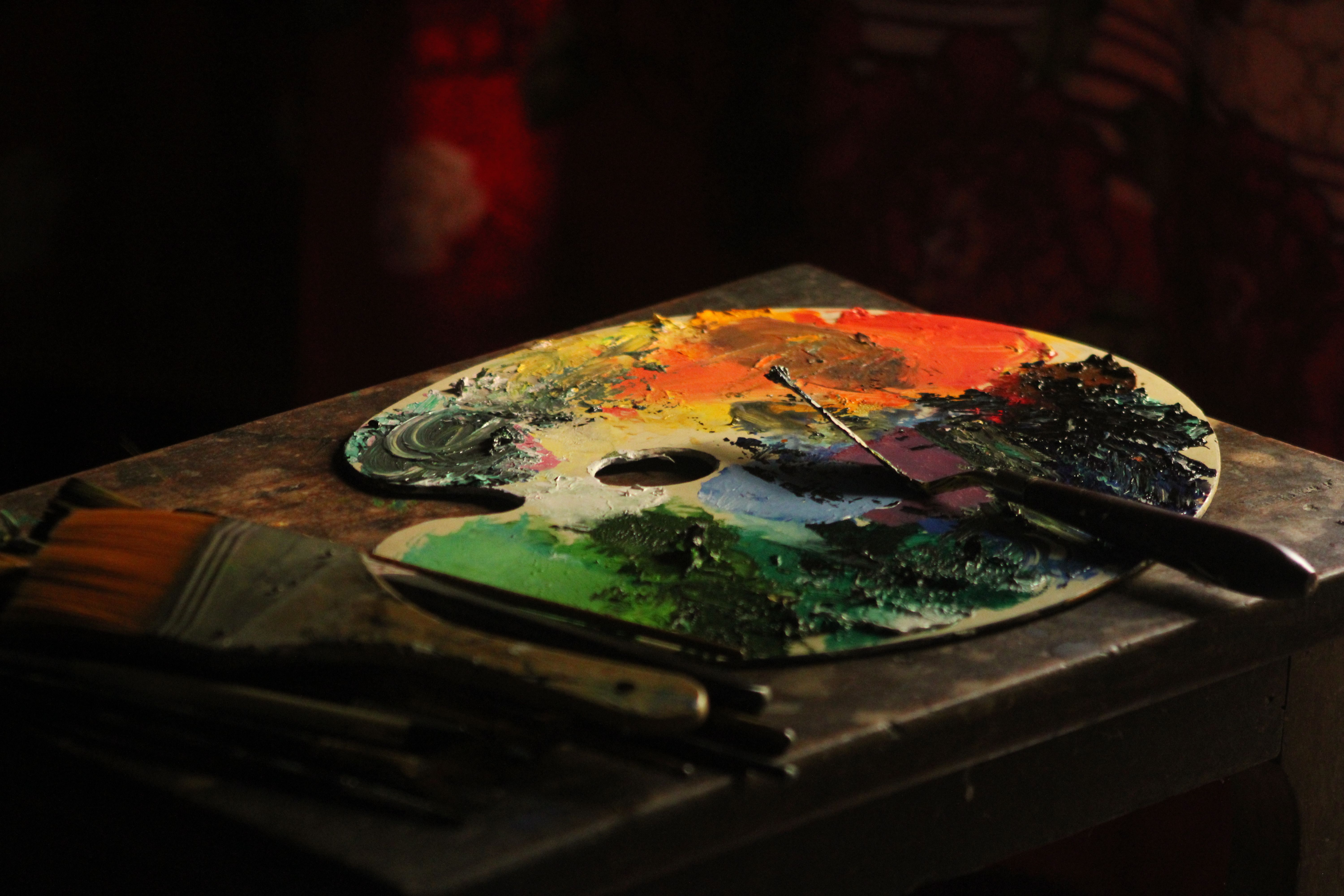 Artistic palette with vibrant colors and brush on a table, in dramatic lighting.