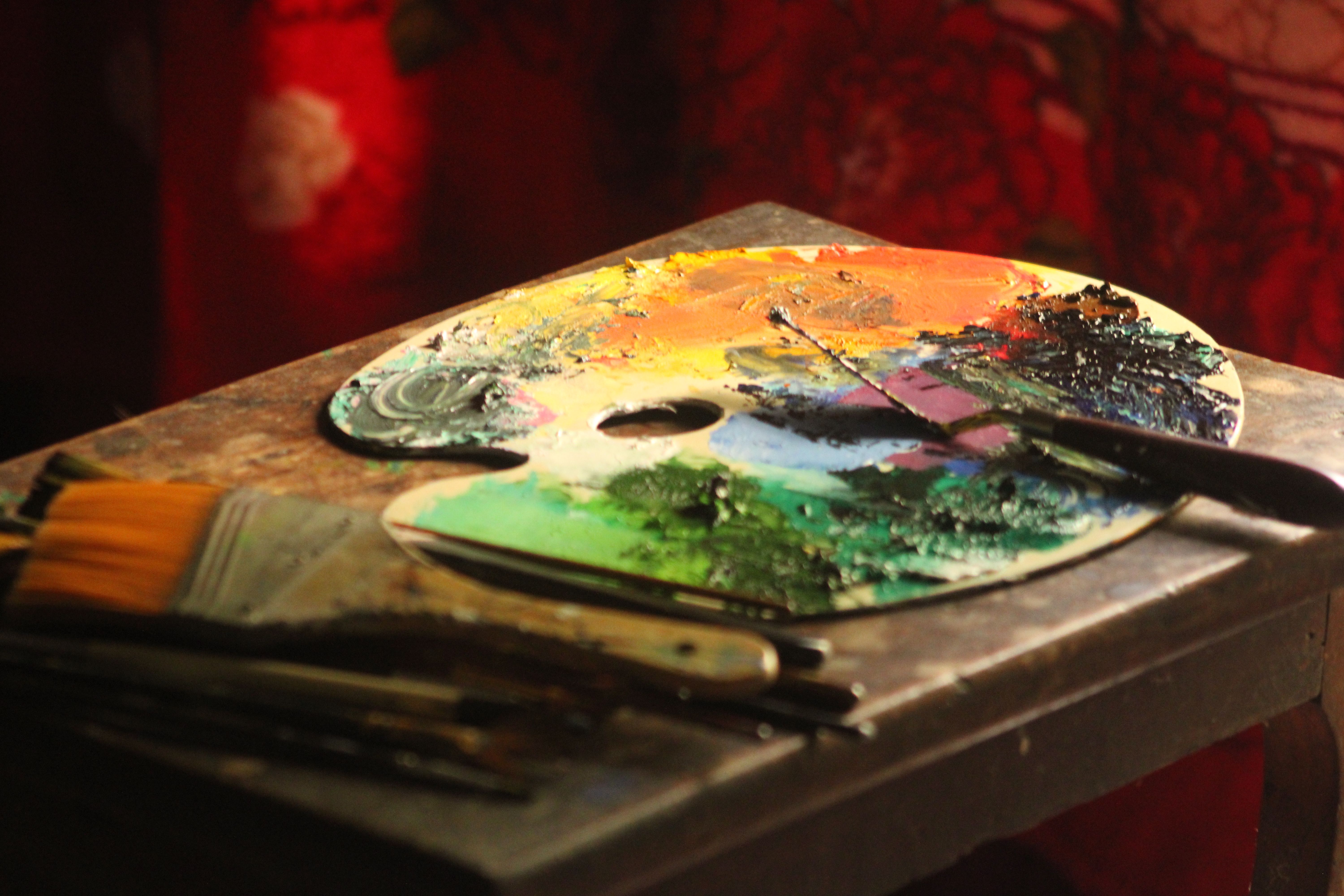 Colorful artist's palette with brushes on a table, bathed in warm light.