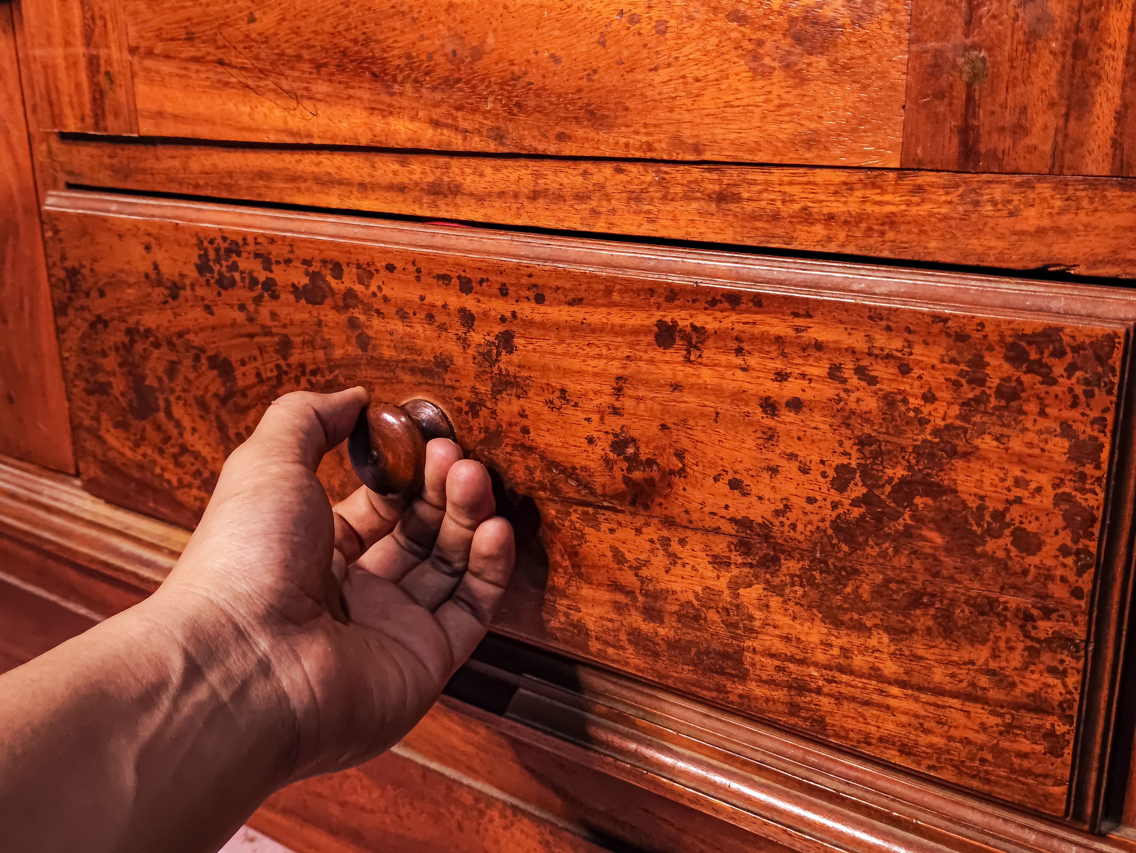 A hand reaches to open a vintage wooden drawer with a rustic patina finish in Pacitan, Indonesia.