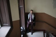 站在楼梯上、手提包放在门口、穿着优雅衣服的帅哥正看着镜头