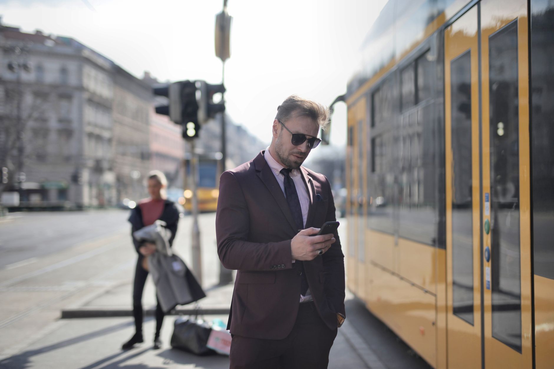 A businessman in corporate attire checks his smartphone at a city tram stop.