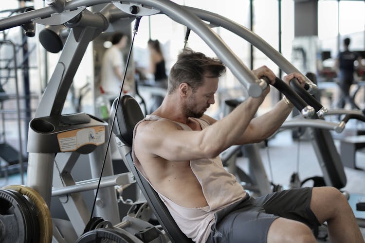 Muscular Man Exercising With Shoulder Press Machine In Gym