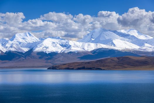 Breathtaking view of snow-covered mountains reflecting in a serene lake under a clear blue sky.