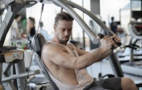 在现代体育中心，一位自信的肌肉男正在肩部压力机上进行锻炼，这是他的侧视图