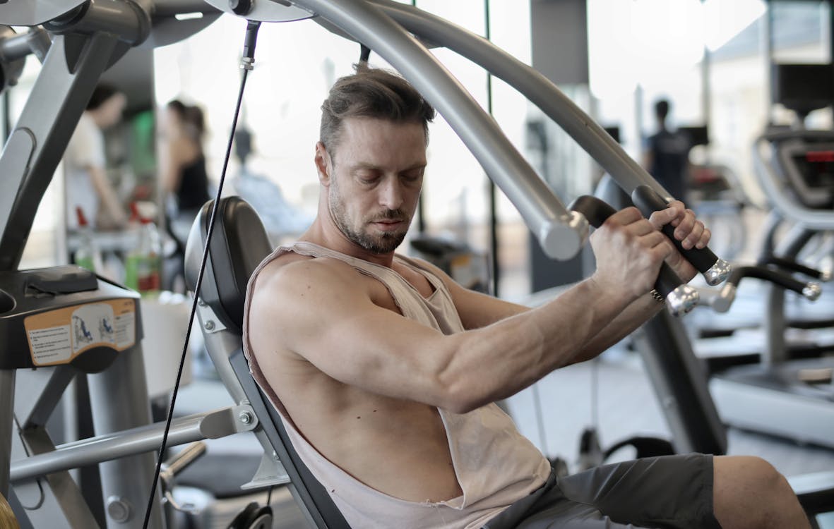 Free Side view of confident muscular man doing exercises on shoulder press machine while training in modern sports center Stock Photo