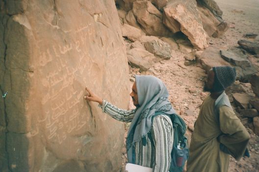 Two men examining historic rock inscriptions in Tabuk, Saudi Arabia.