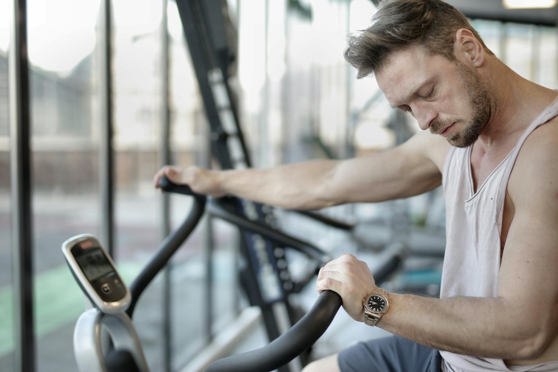 Side view of weary male athlete in activewear doing cardio exercises on sports equipment in modern fitness center