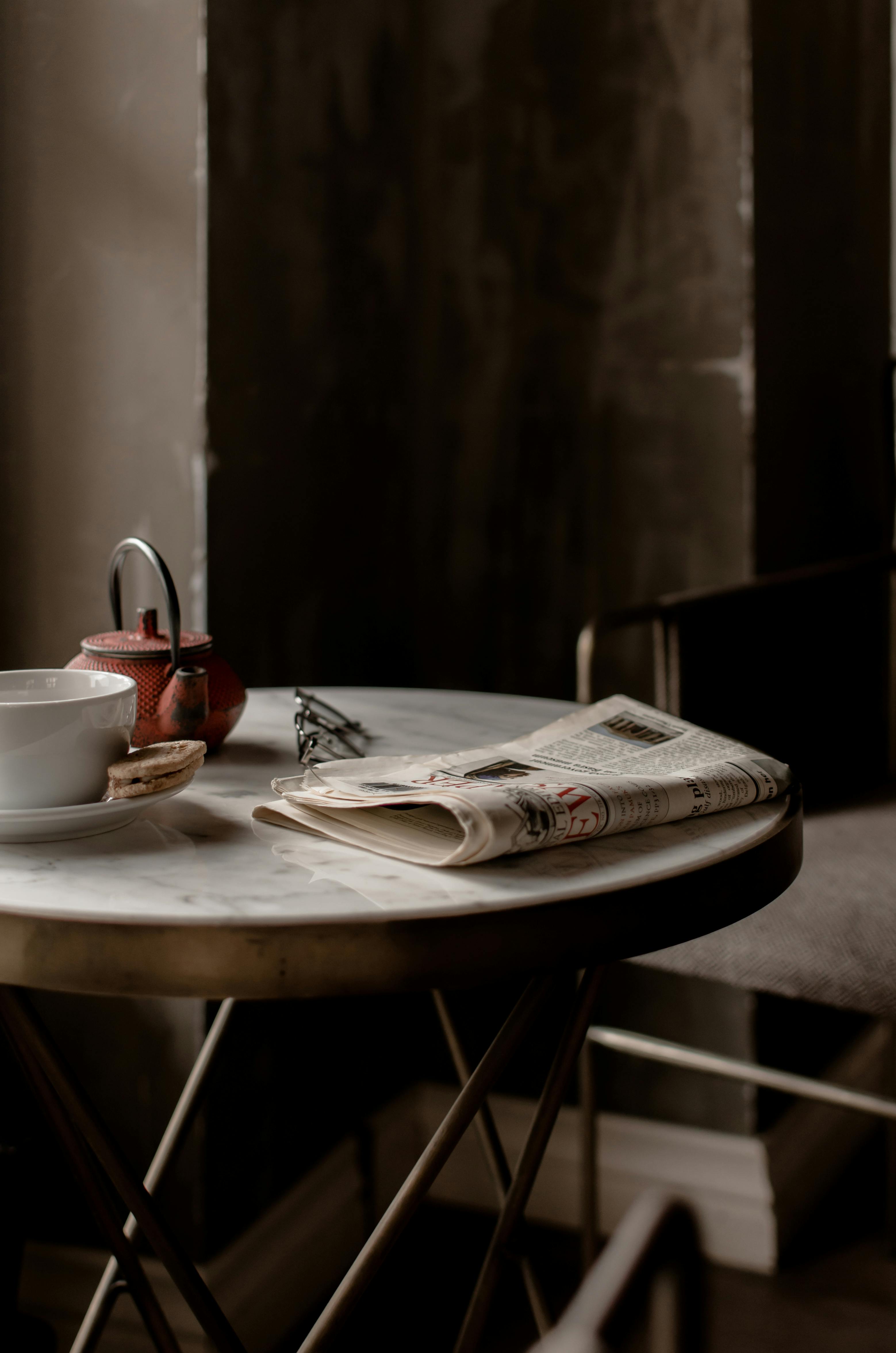 tea set and newspaper placed on round table near comfortable chair