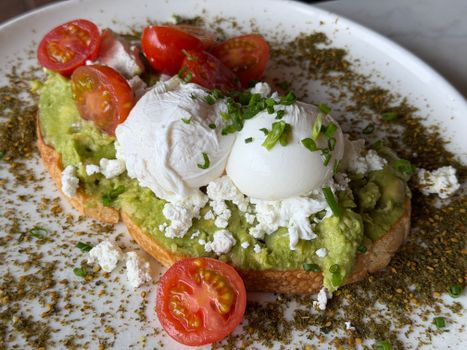 Gourmet avocado toast topped with poached eggs, cherry tomatoes, and cheese garnished with herbs.