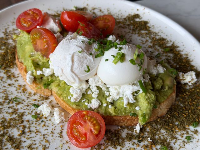 Gourmet avocado toast topped with poached eggs, cherry tomatoes, and cheese garnished with herbs.