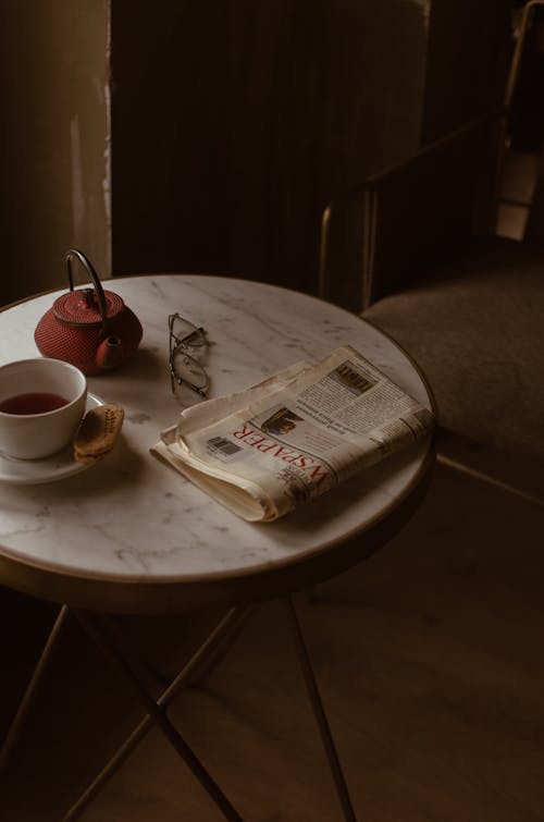 Free From above of round marble textured table with tea set placed near newspaper and eyeglasses in retro style cafe Stock Photo