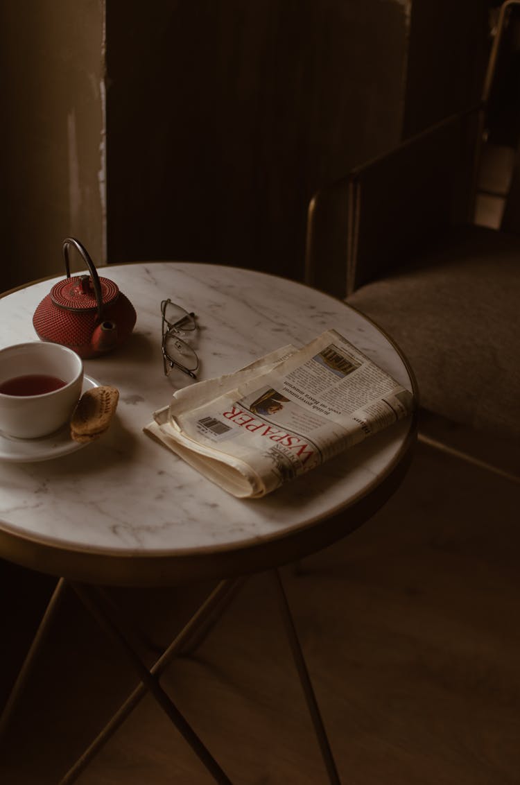 Comfortable Chair Near Round Table With Newspaper And Tea Set