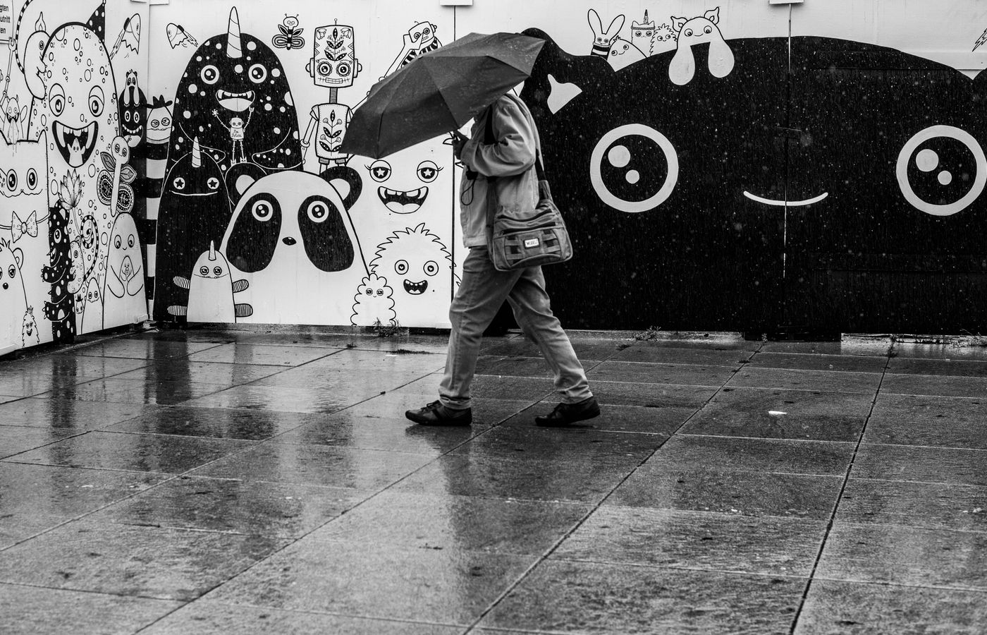 A person walking with an umbrella in a rainy urban area, featuring artistic wall art.