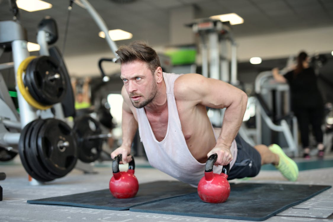 influencer Free Low angle of strong sportsman making effort and pushing up on metal kettlebells during workout in modern gym and looking away Stock Photo