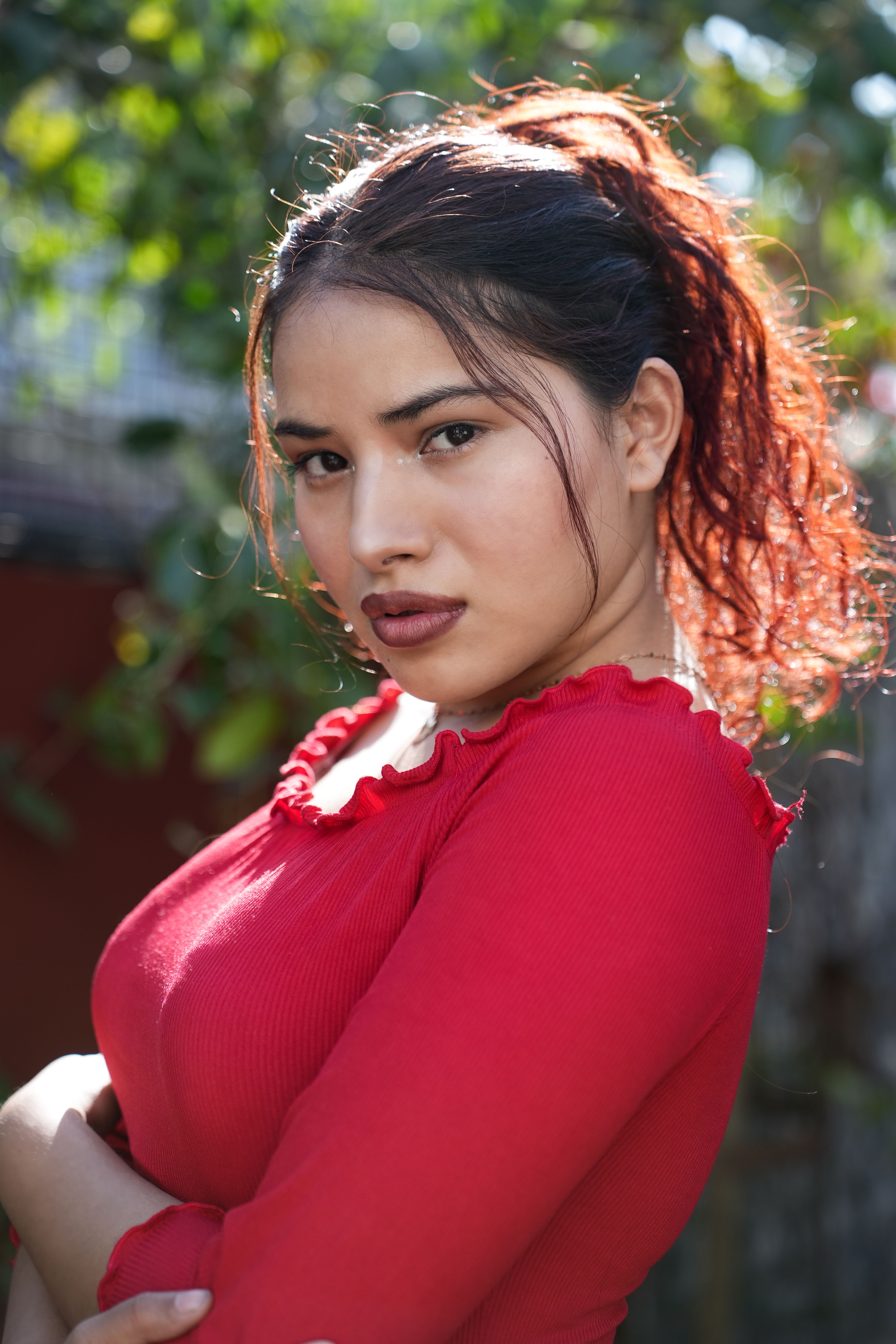 Captivating portrait of a confident woman in a red outfit, with natural lighting outdoors.