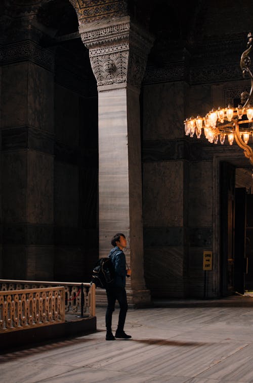 Side view of unrecognizable young male traveler in casual clothes with backpack admiring ancient palace during sightseeing tour