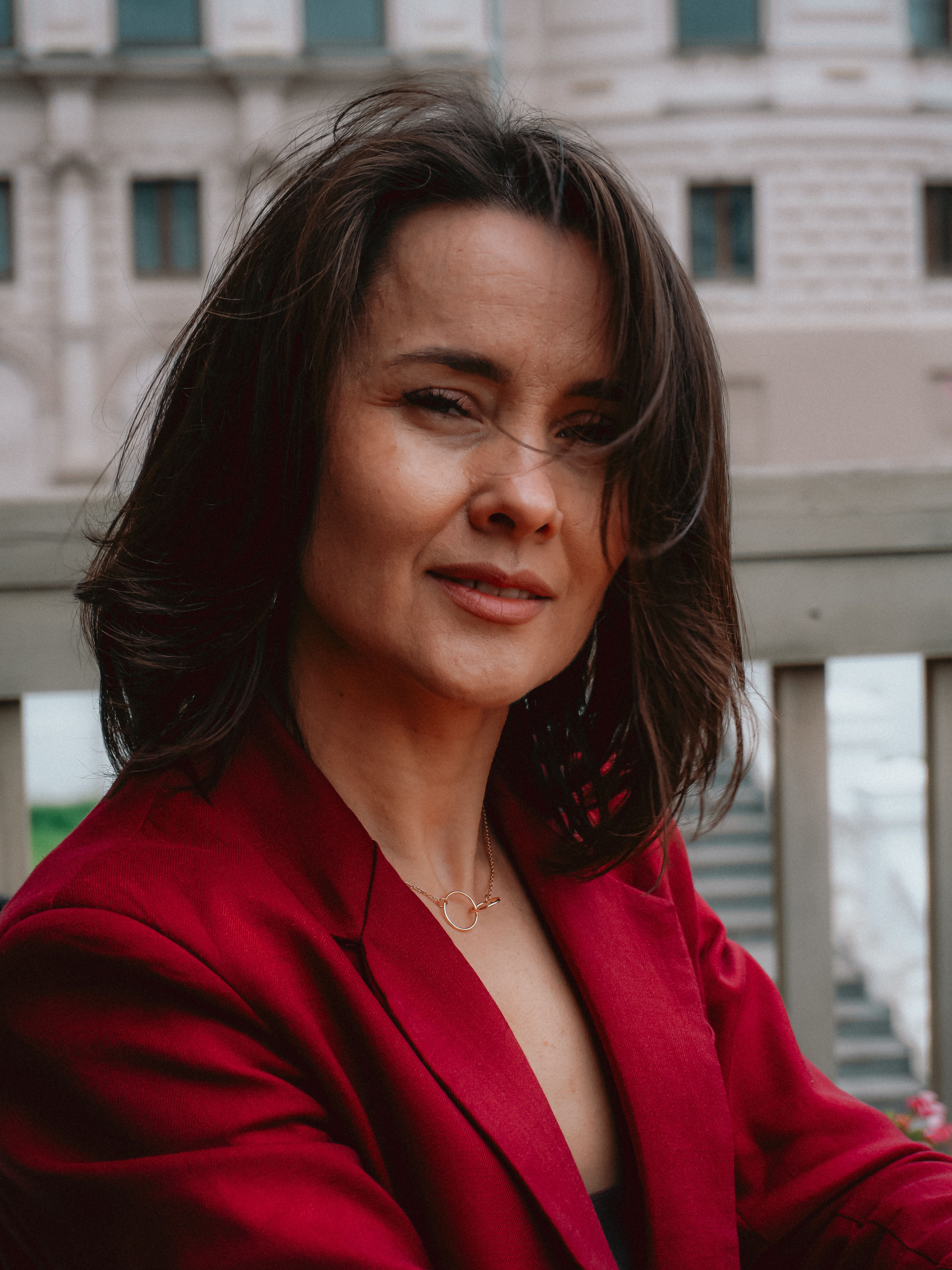 Portrait of a confident woman wearing a red blazer outdoors. Urban backdrop adds depth.
