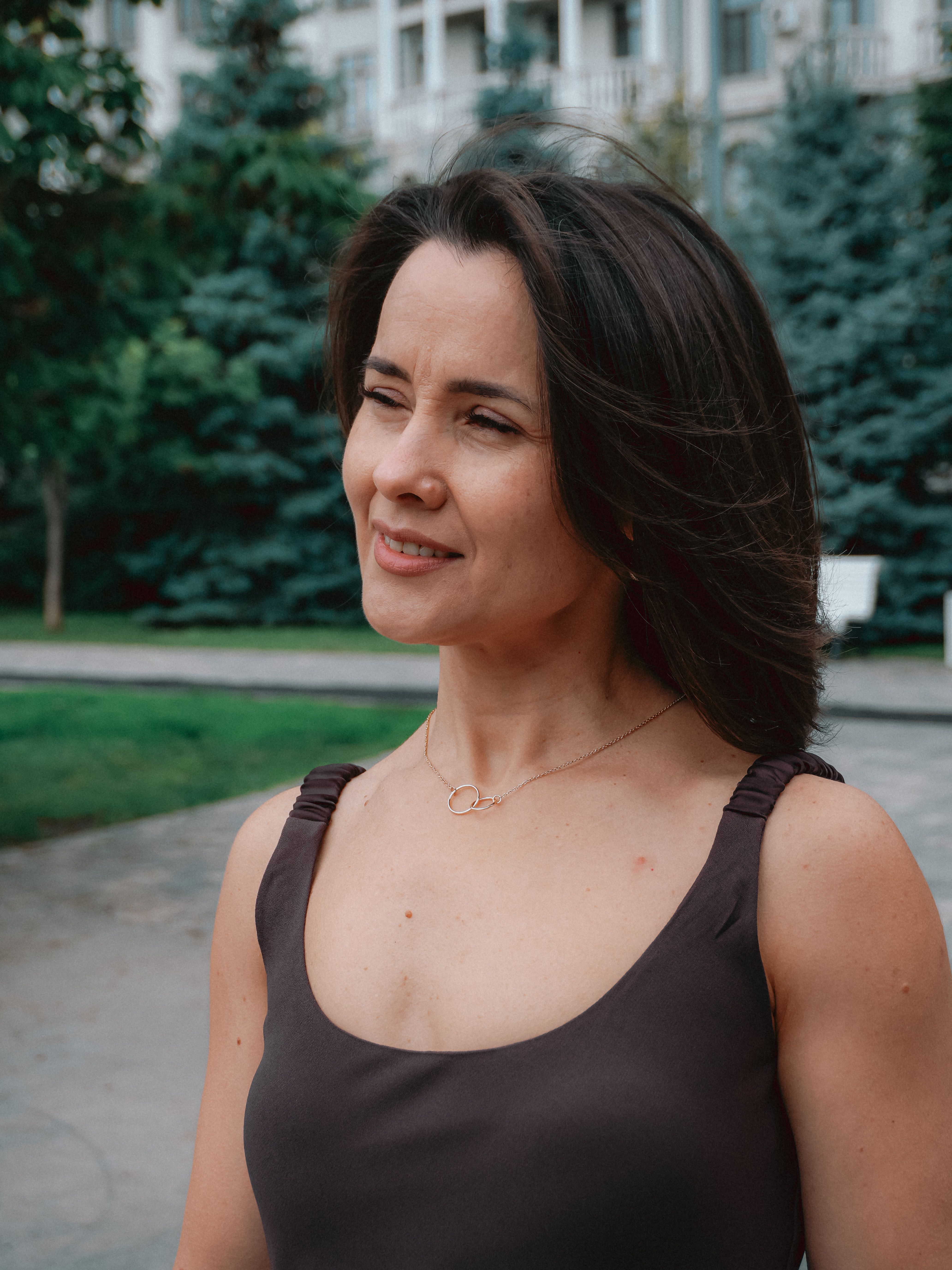 Portrait of a confident woman outdoors with greenery and architecture.