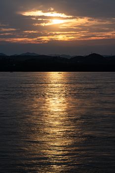 A tranquil scene capturing a golden sunset reflecting over a calm river with distant hills.