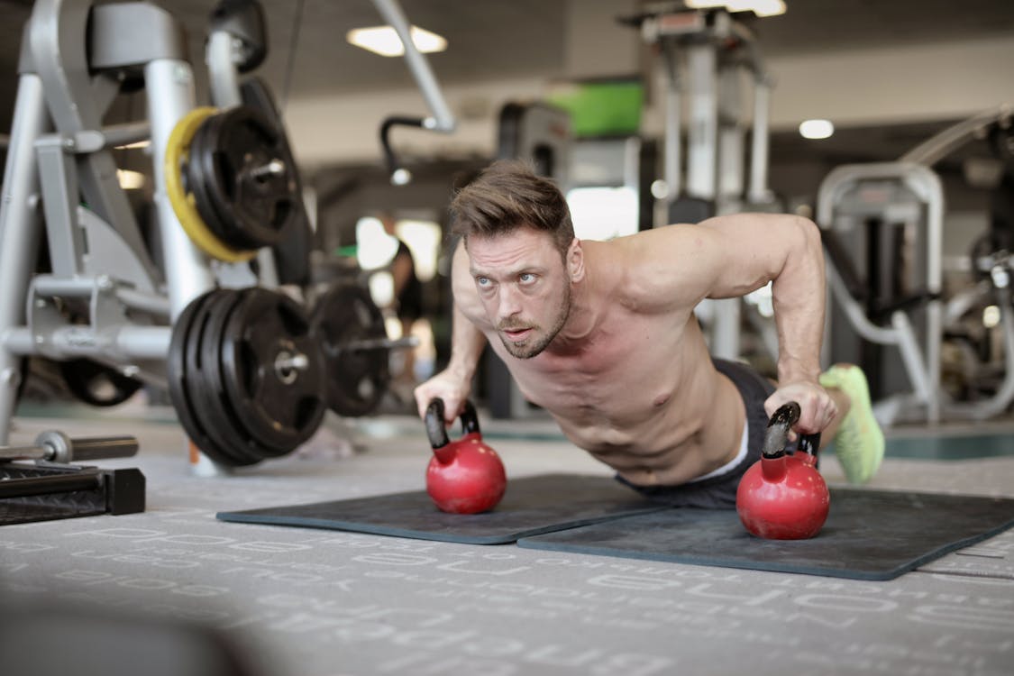 Free Serious muscular sportsman doing push ups on kettlebells in modern gym Stock Photo
