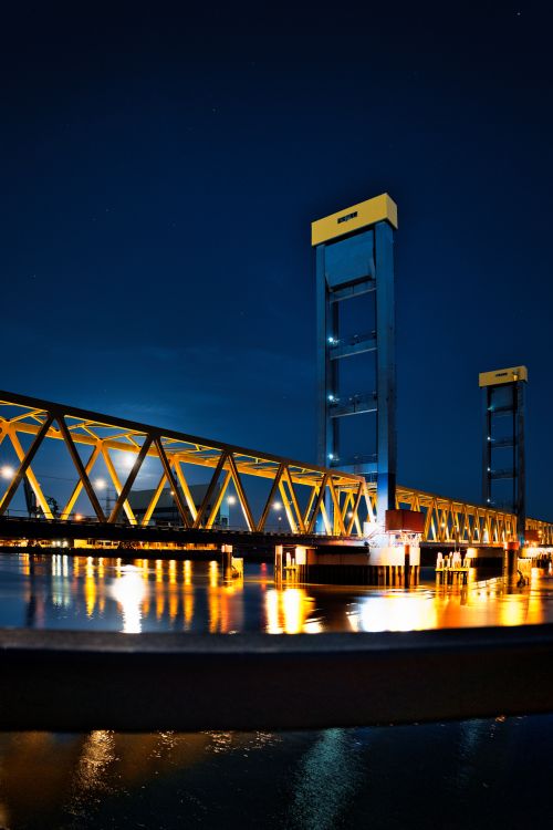 Free Night view of a brightly lit bridge reflecting on water, creating a mesmerizing scene. Stock Photo