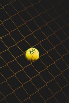 A close-up of a bright yellow tennis ball wedged in a net against a moody dark background.
