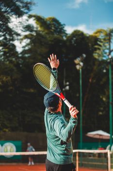 A man in a cap serves a tennis ball during a match on an outdoor court.