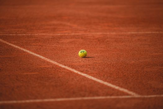 A lone tennis ball rests on a red clay tennis court, highlighting its vibrant texture.