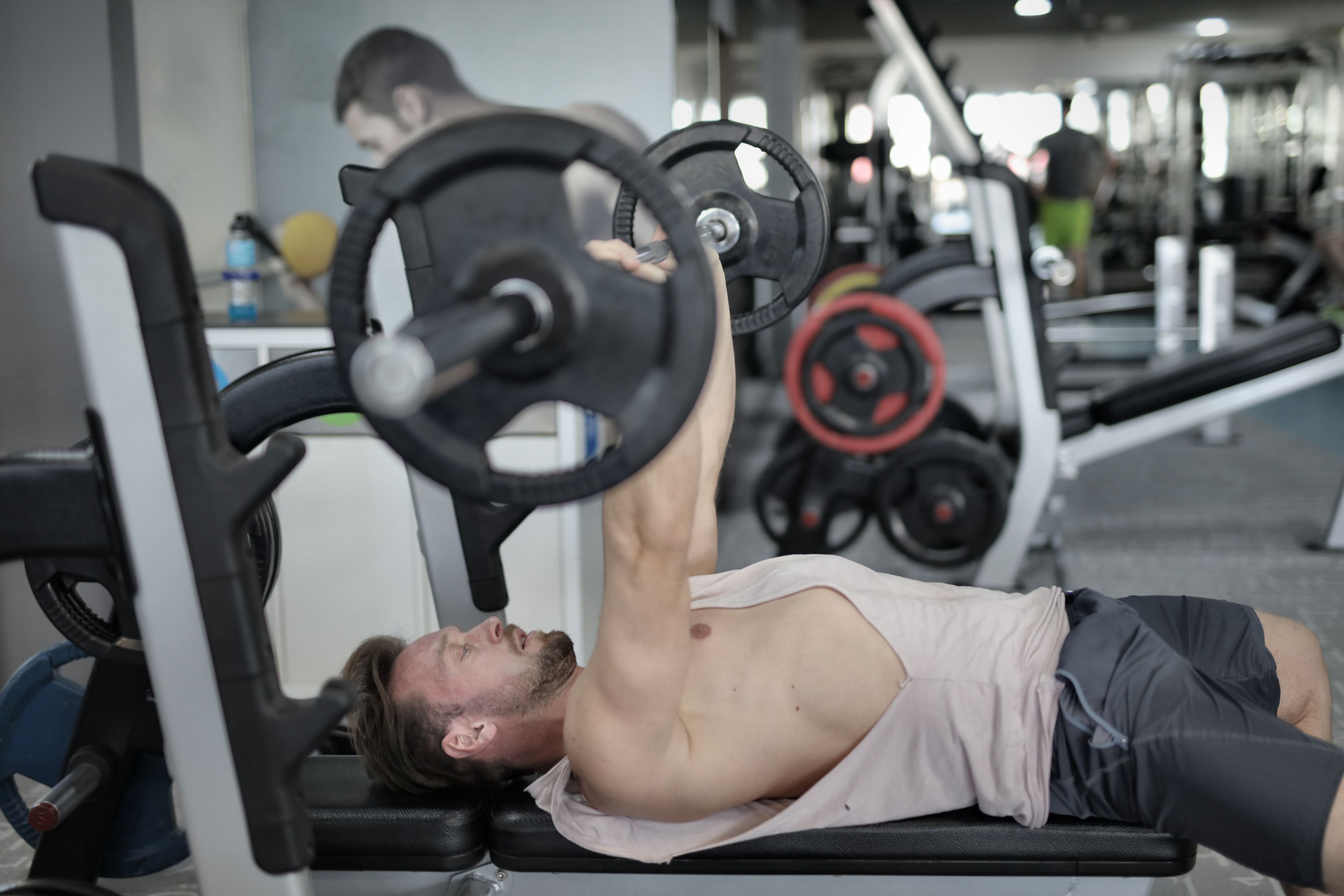 Side view of strong young sportsman in sportswear lying on bench and pressing heavy barbell doing chest exercise training in modern gym