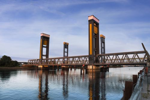 Free A modern drawbridge reflects over a calm river during daylight. Stock Photo