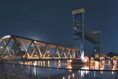 Free A luminous modern bridge stretches over a peaceful river at night, showcasing architectural elegance and serene reflections. Stock Photo