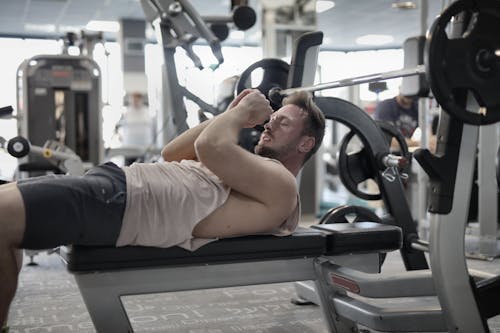 Free Focused muscular sportsman in modern sportswear preparing to workout with heavy barbell on bench training in modern gym Stock Photo