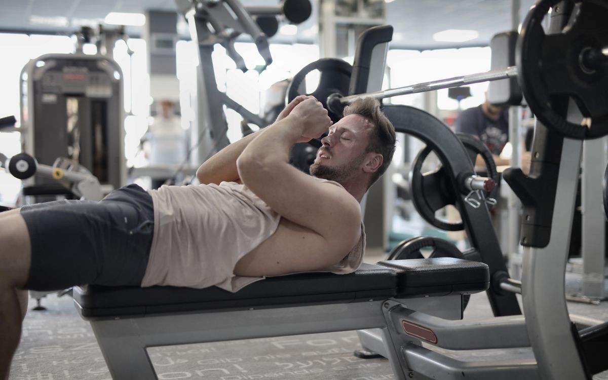 Focused muscular sportsman in modern sportswear preparing to workout with heavy barbell on bench training in modern gym