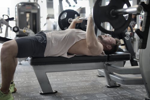 Strong sportsman working out on bench in modern gym