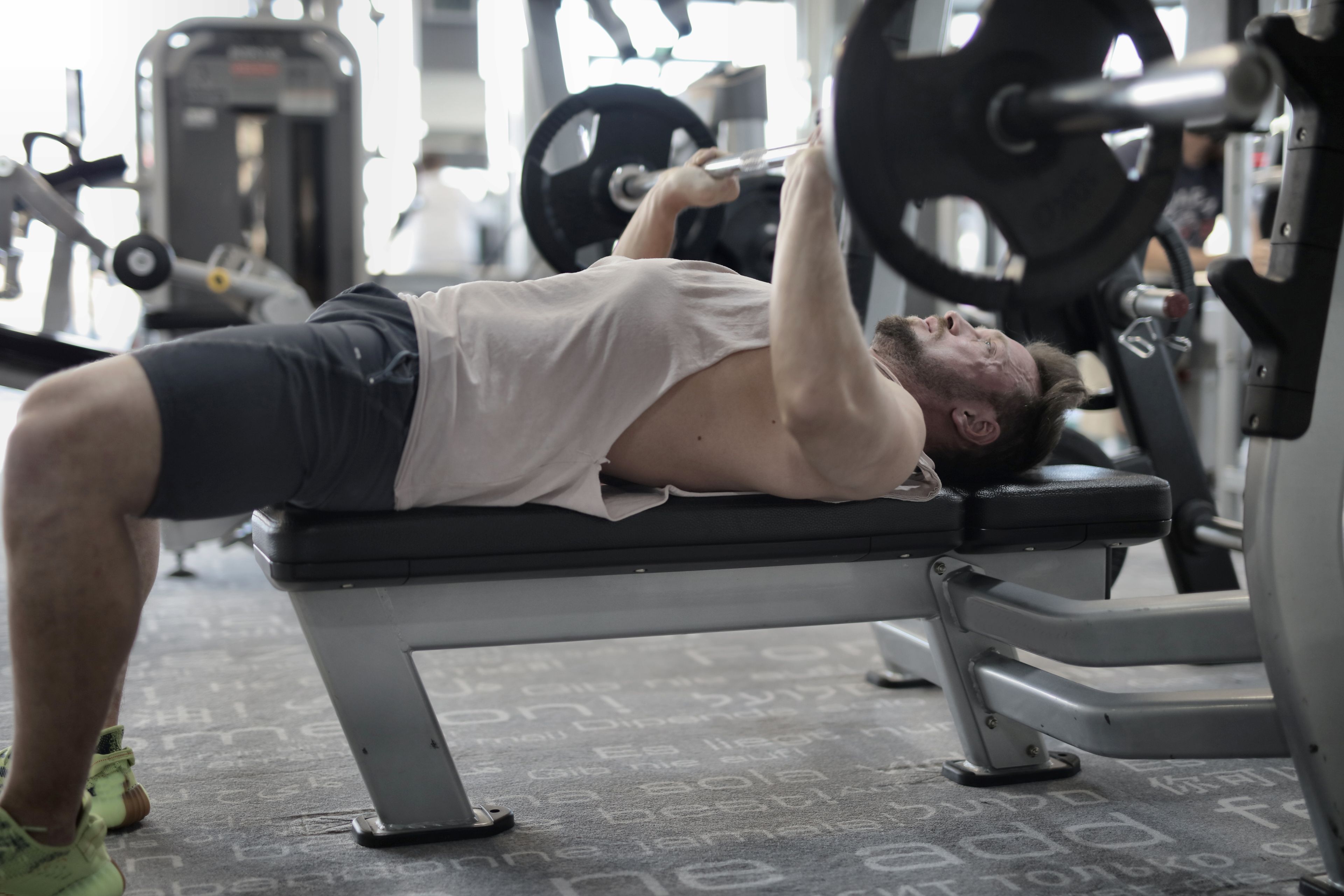 Side view of strong muscular sportsman in sportswear performing weightlifting exercise with heavy barbell on bench during intense workout in gym