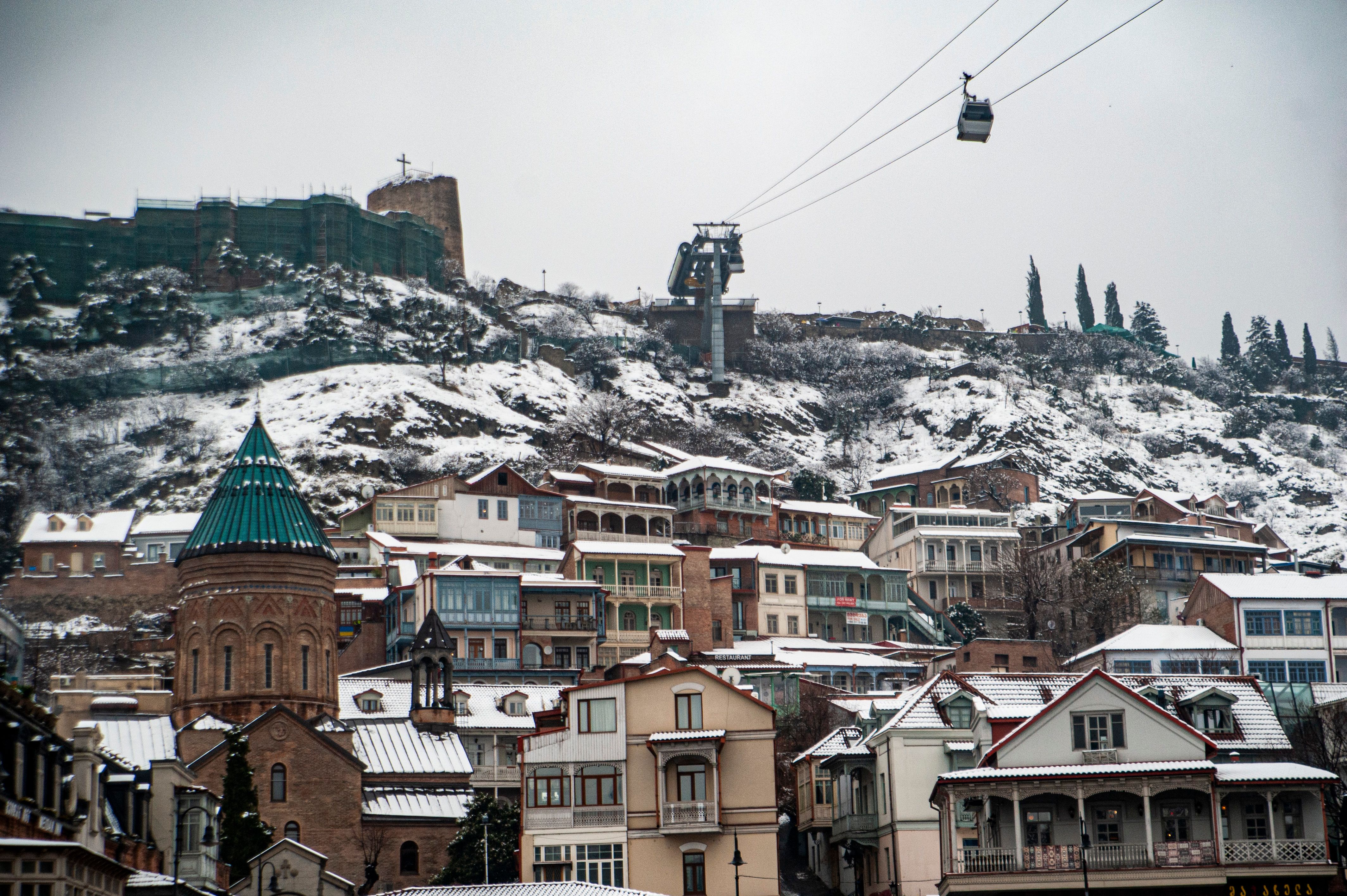 Scenic winter view of Tbilisi, Georgia with snow-covered rooftops and cable car in the background.