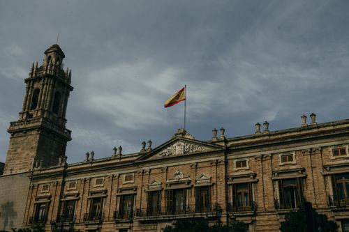 Free Historic government building in Valencia with a Spanish flag on top against a cloudy sky. Stock Photo